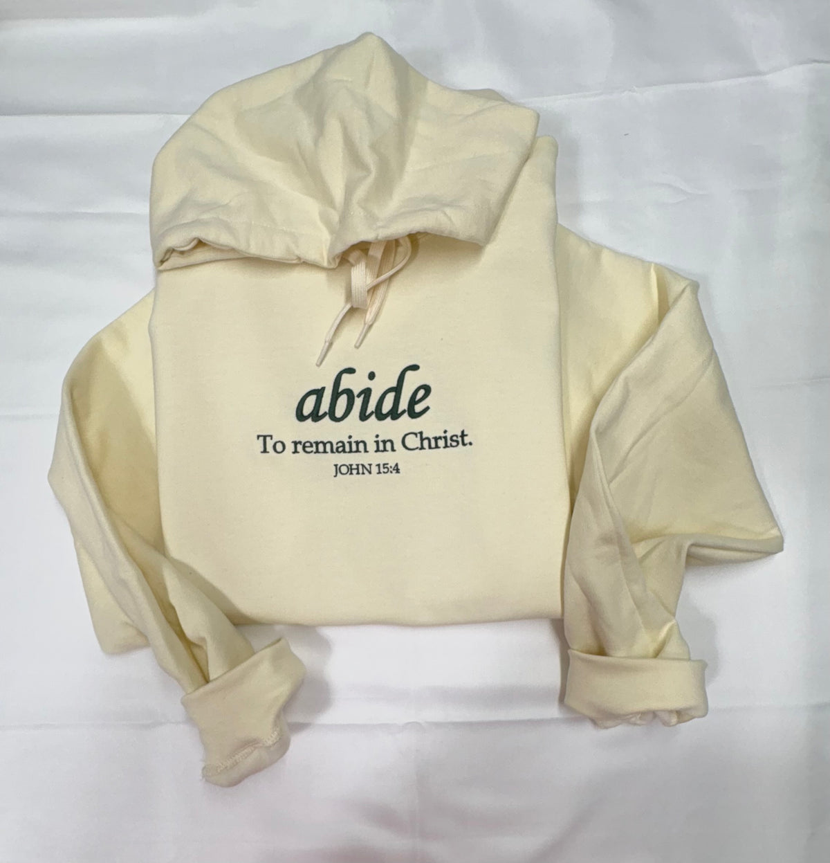 Pale yellow hoodie with dark lettering reading abide, To remain in Christ, John 15:4