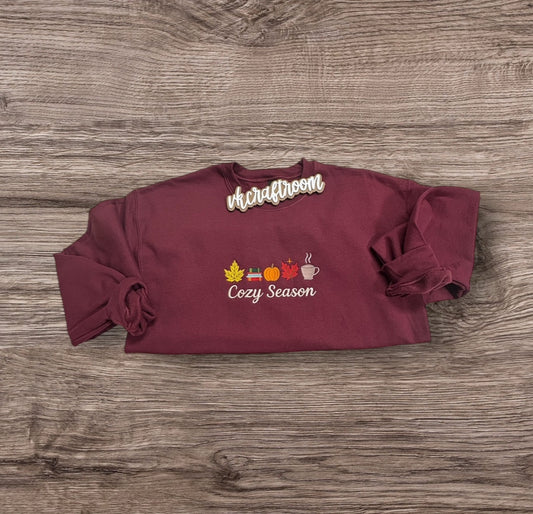 Burgundy Cozy Season embroidered sweatshirt with leaves, books, a pumpkin, and a steaming mug