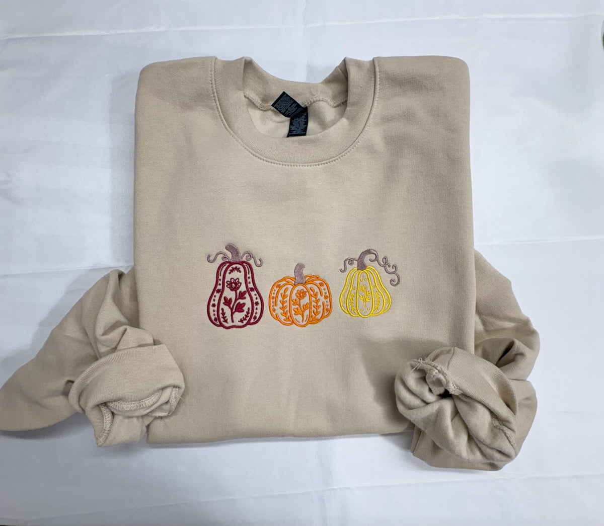 Beige crewneck sweatshirt embroidered with three floral pumpkins in burgundy, orange, and yellow