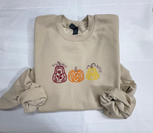 Beige crewneck sweatshirt embroidered with three floral pumpkins in burgundy, orange, and yellow
