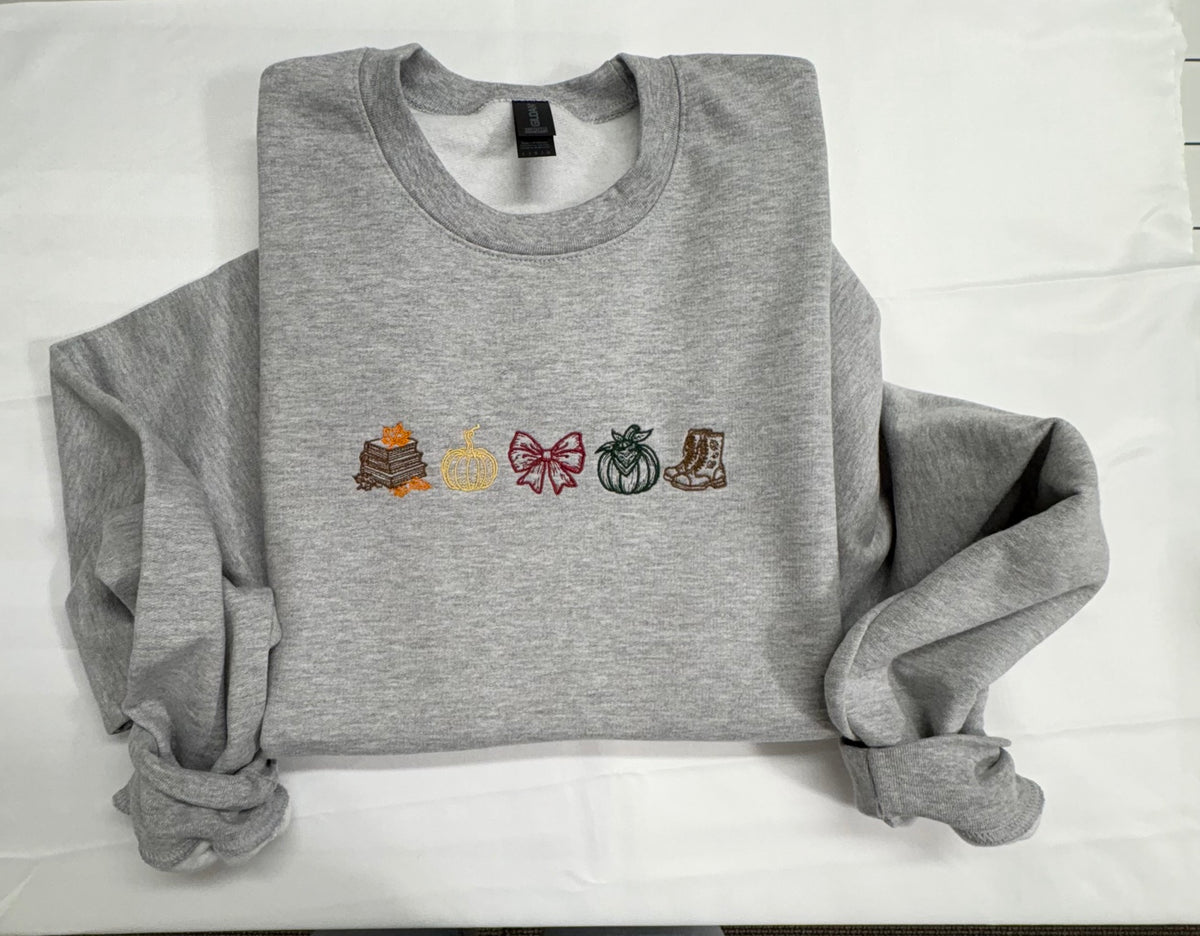 Heather gray crewneck sweatshirt embroidered with books and autumn leaves, two pumpkins, a burgundy bow, and boots