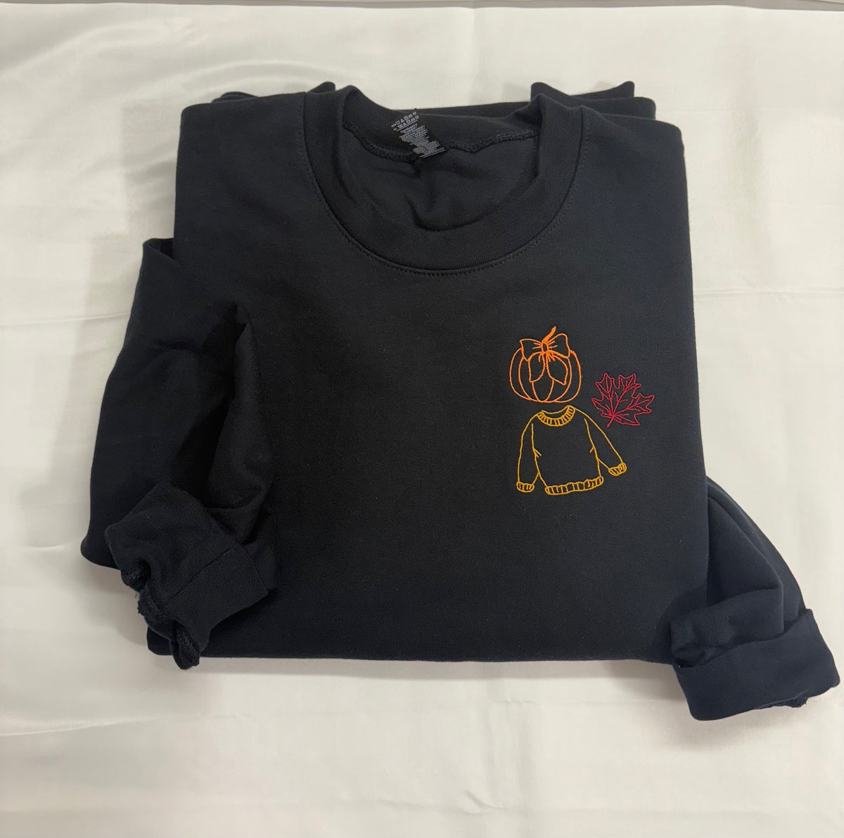 Black crewneck sweatshirt with a left chest embroidered orange pumpkin and bow, golden yellow sweater, and burgundy maple leaf