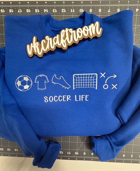 Royal blue youth sweatshirt with white Soccer Life embroidery, soccer ball, jersey, cleat, goal, and play diagram